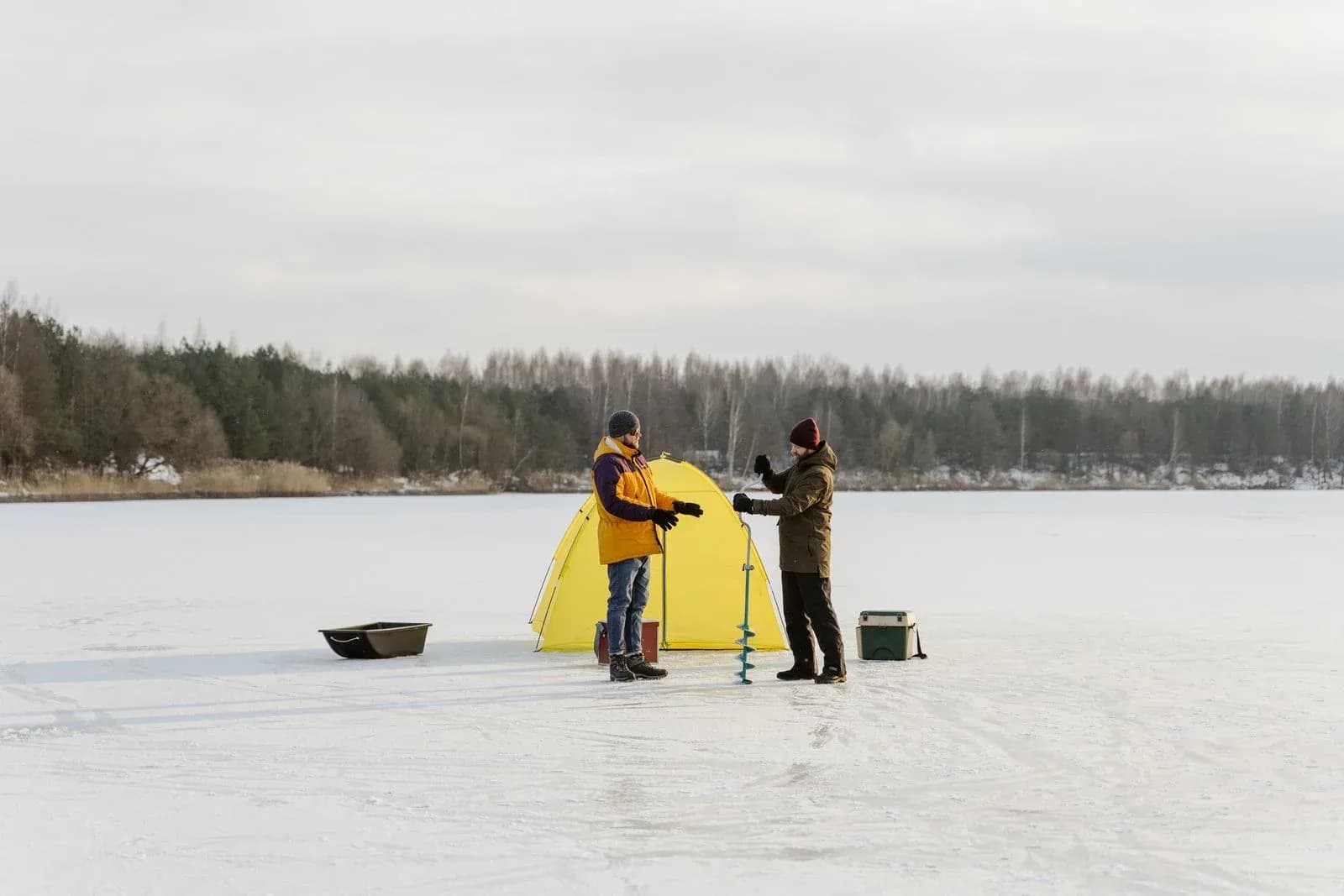 Två isfiskare med ett gult tält på en frusen sjö