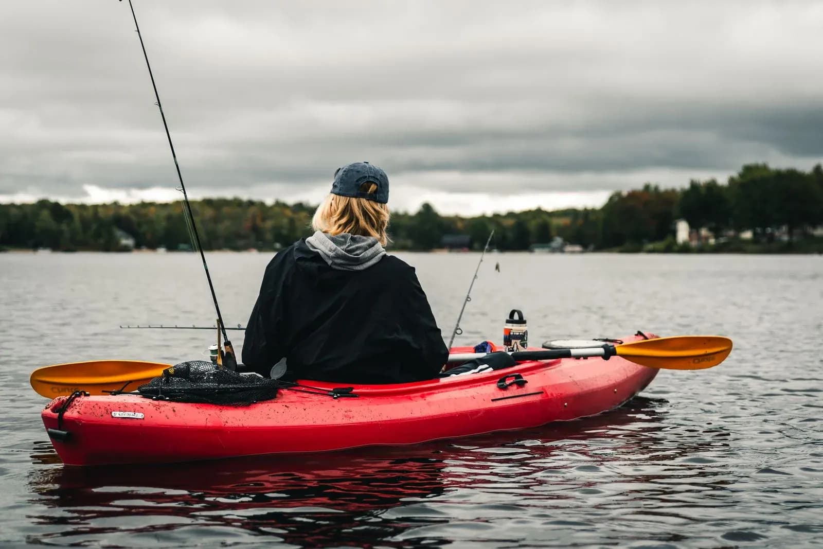 Fiskare i en röd kajak på en sjö under mulen himmel