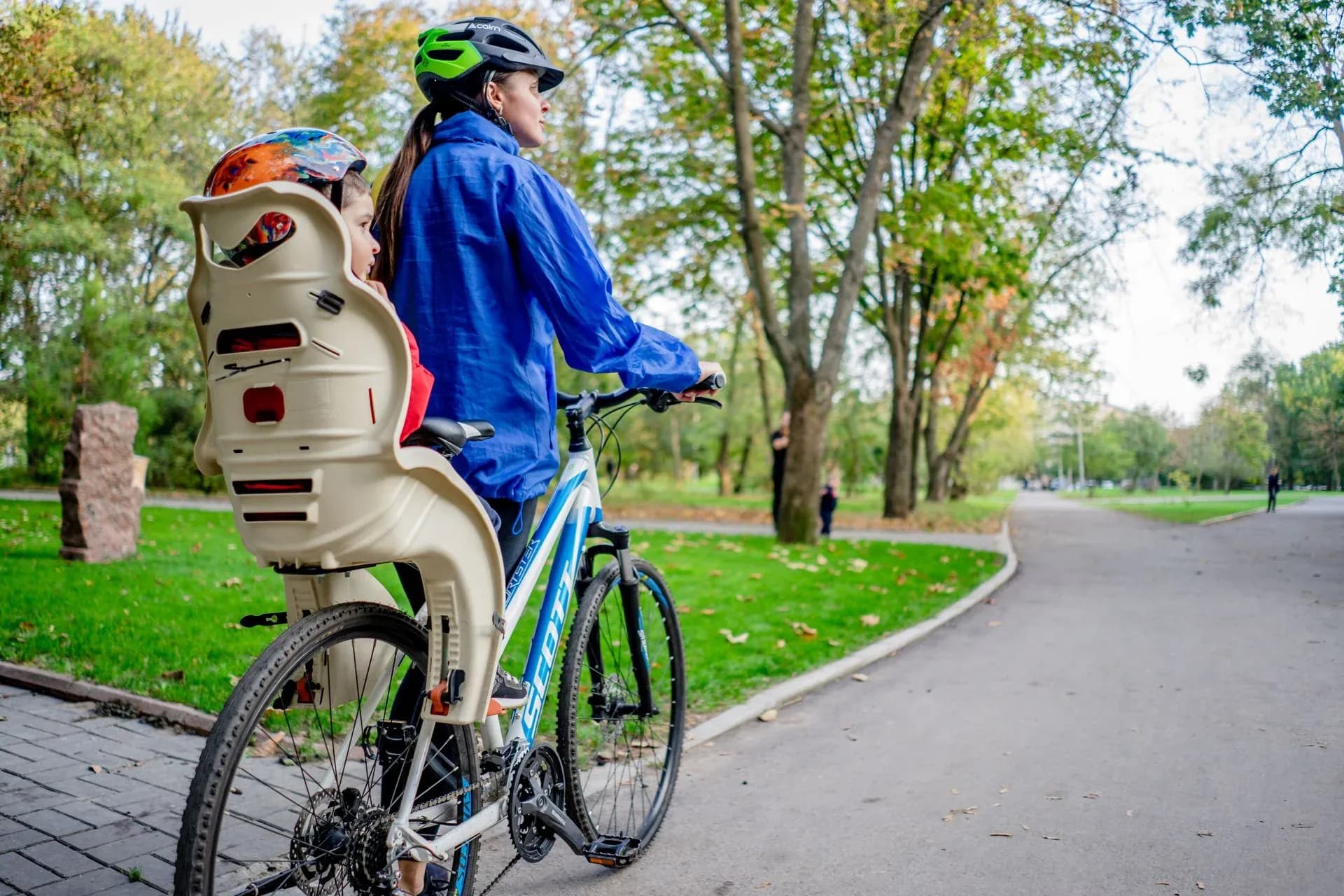 Kvinna som cyklar i en park med ett barn i cykelbarnstol bak