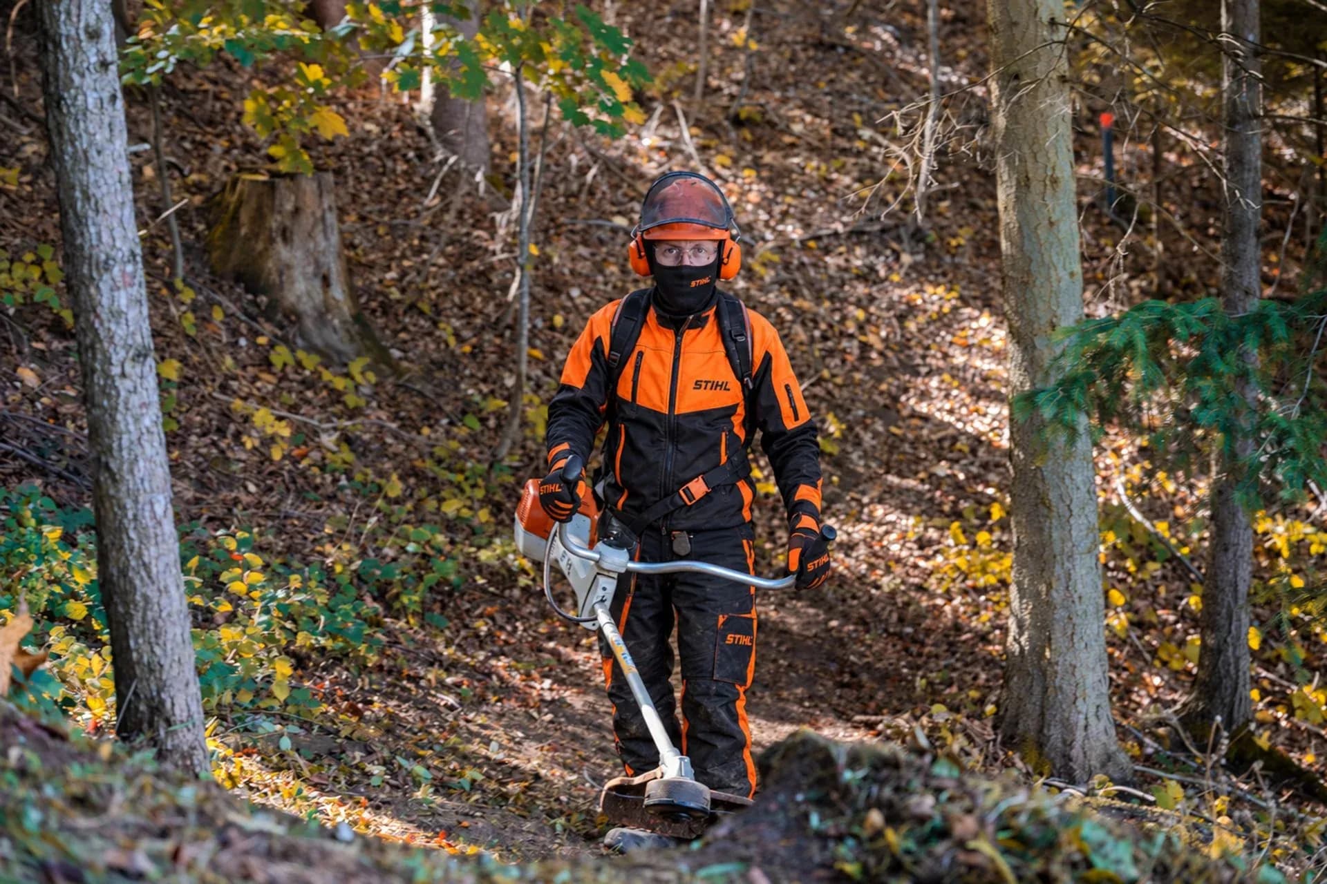 Skogsarbetare i orange skyddskläder med röjsåg i höstskogen
